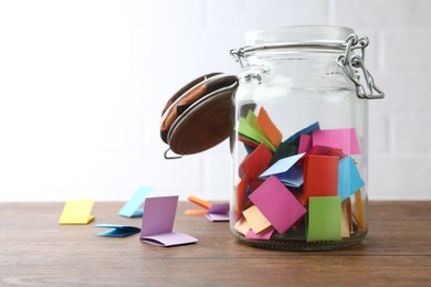 Photo of Jar with colorful pieces of paper on wooden table near white brick wall. Space for text