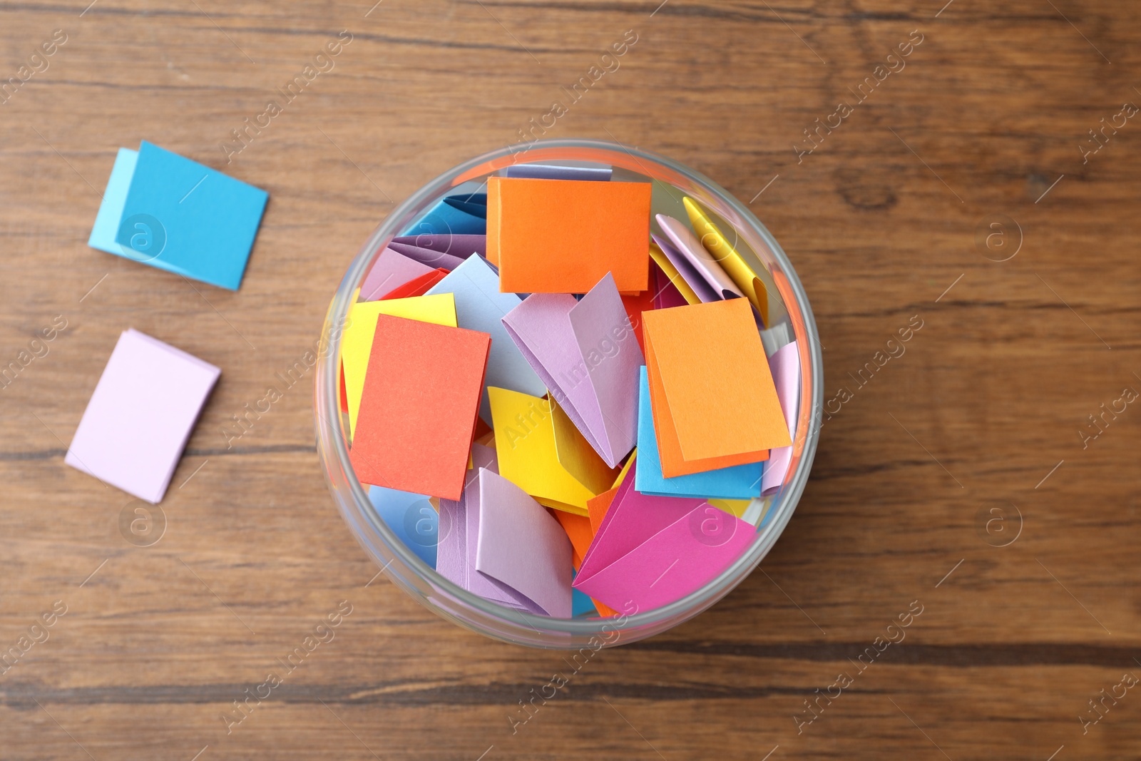 Jar with colorful pieces of paper on wooden table, top view Photo of Jar with colorful pieces of paper on wooden table, top view