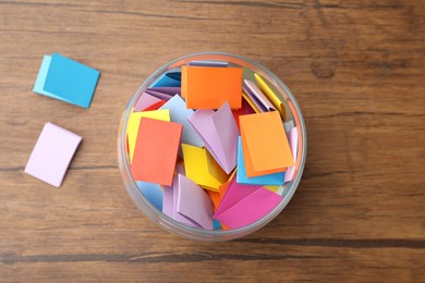 Photo of Jar with colorful pieces of paper on wooden table, top view