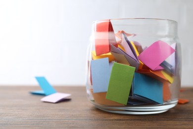 Photo of Jar with colorful pieces of paper on wooden table near white brick wall, closeup. Space for text