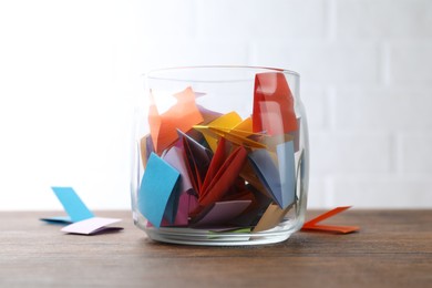 Photo of Jar with colorful pieces of paper on wooden table near white brick wall, closeup