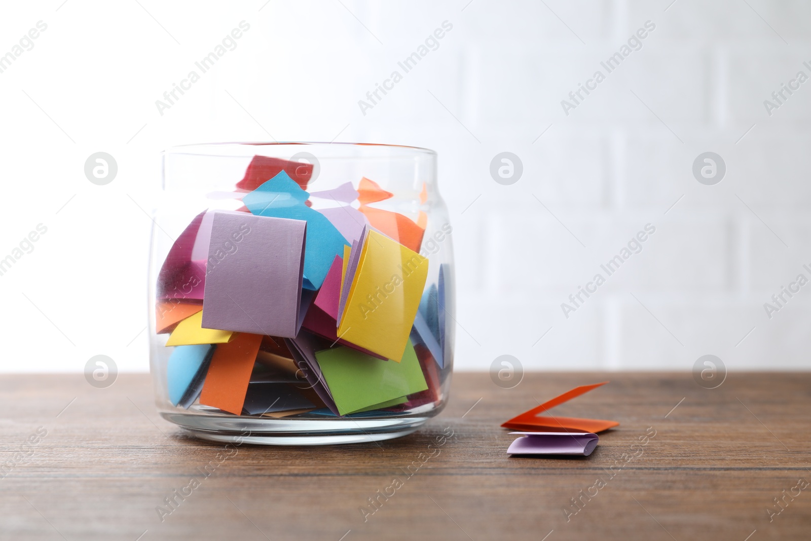 Photo of Jar with colorful pieces of paper on wooden table near white brick wall. Space for text