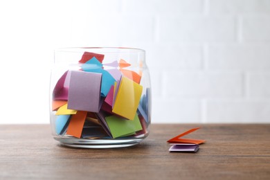 Photo of Jar with colorful pieces of paper on wooden table near white brick wall. Space for text