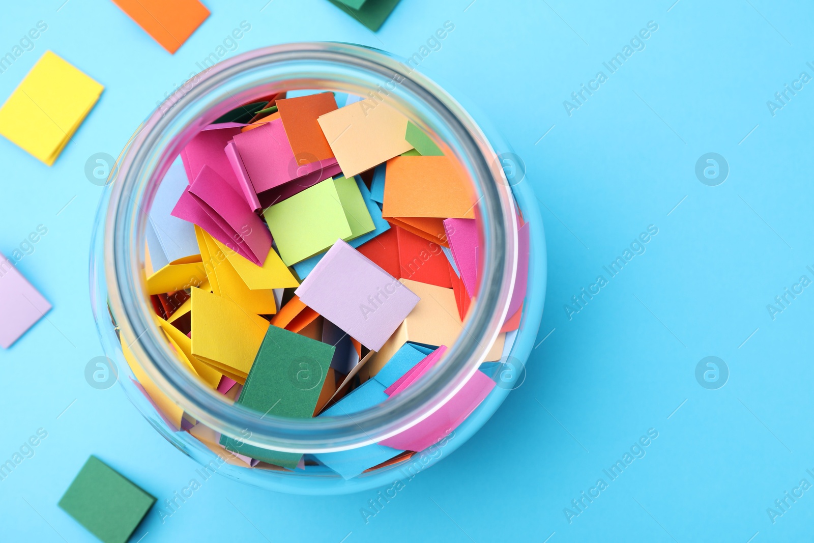 Photo of Jar with colorful pieces of paper on light blue background, flat lay