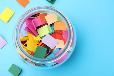 Photo of Jar with colorful pieces of paper on light blue background, flat lay