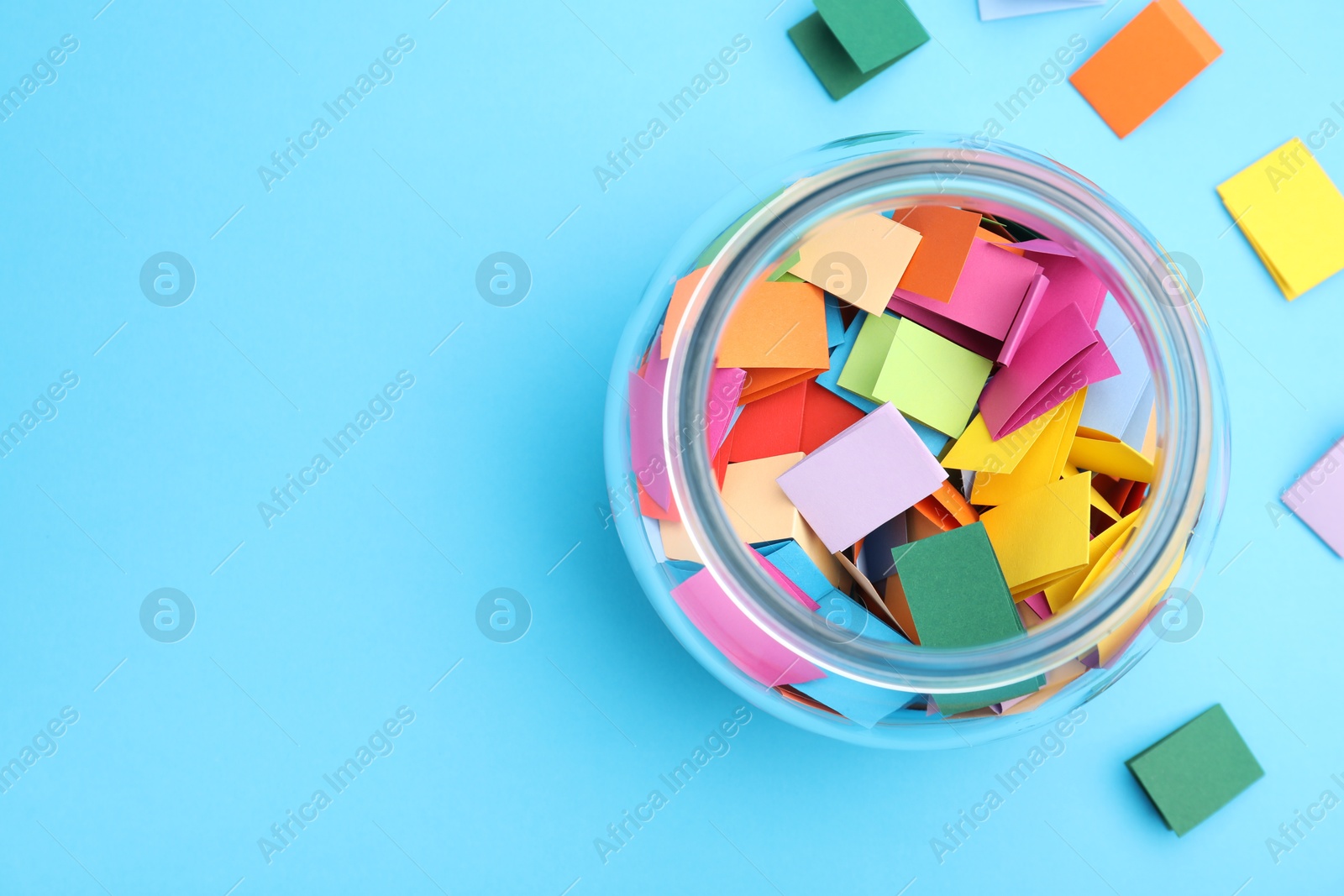 Jar with colorful pieces of paper on light blue background, flat lay. Space for text Photo of Jar with colorful pieces of paper on light blue background, flat lay. Space for text