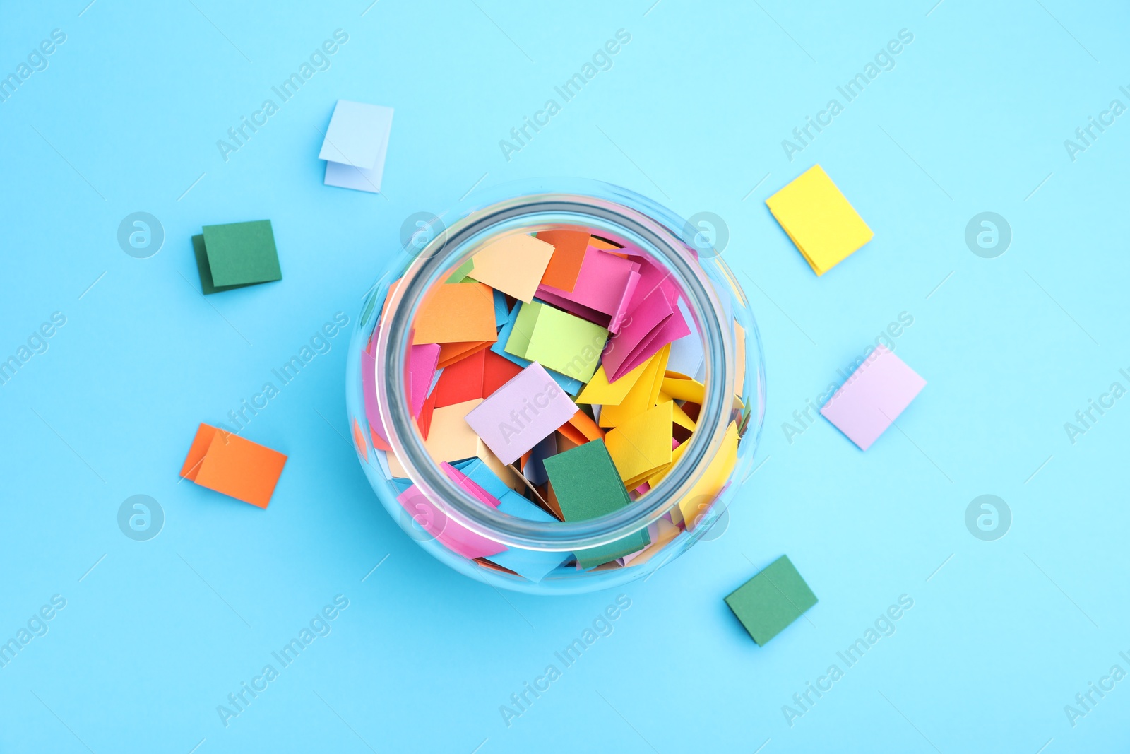 Jar with colorful pieces of paper on light blue background, flat lay Photo of Jar with colorful pieces of paper on light blue background, flat lay