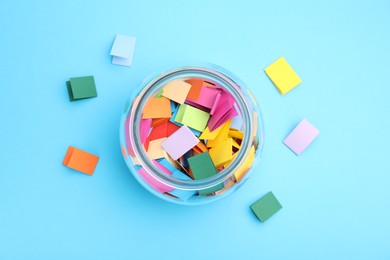 Photo of Jar with colorful pieces of paper on light blue background, flat lay