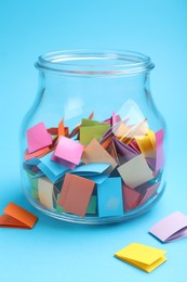 Photo of Jar with colorful pieces of paper on light blue background, closeup