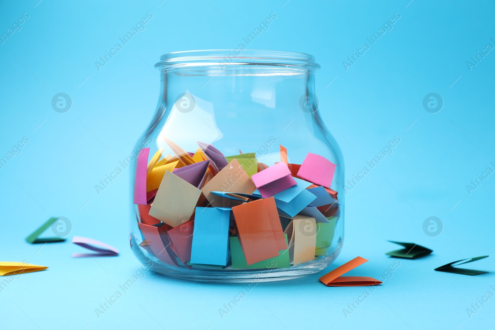 Jar with colorful pieces of paper on light blue background, closeup Photo of Jar with colorful pieces of paper on light blue background, closeup