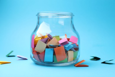 Photo of Jar with colorful pieces of paper on light blue background, closeup