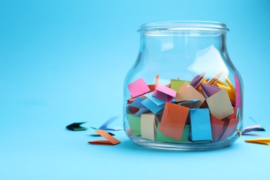 Photo of Jar with colorful pieces of paper on light blue background, closeup. Space for text