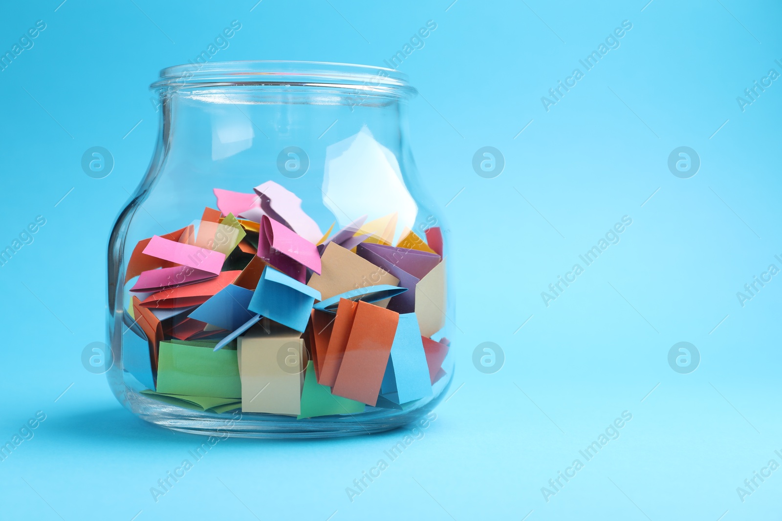 Jar with colorful pieces of paper on light blue background, closeup. Space for text Photo of Jar with colorful pieces of paper on light blue background, closeup. Space for text