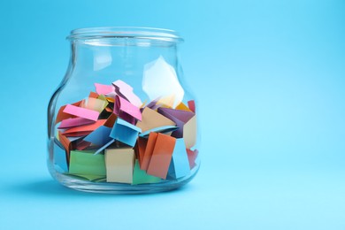 Photo of Jar with colorful pieces of paper on light blue background, closeup. Space for text