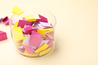 Photo of Jar with colorful pieces of paper on beige background, closeup. Space for text