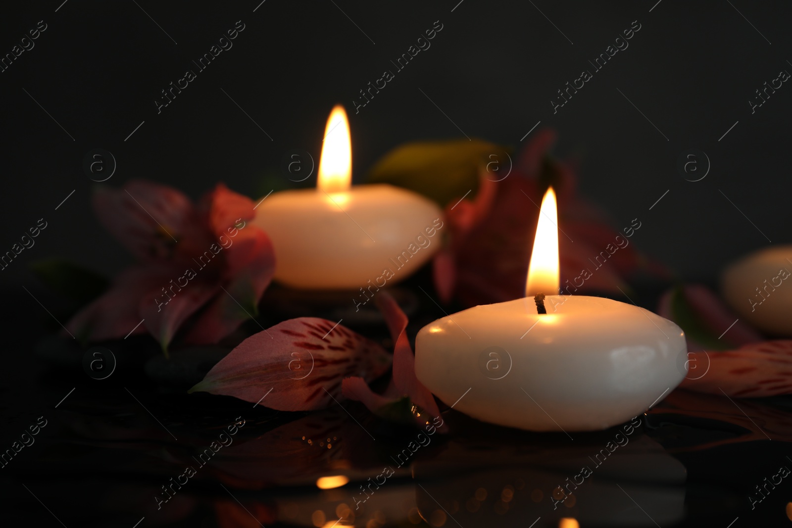 Burning candles and beautiful flowers on wet black table, closeup Photo of Burning candles and beautiful flowers on wet black table, closeup