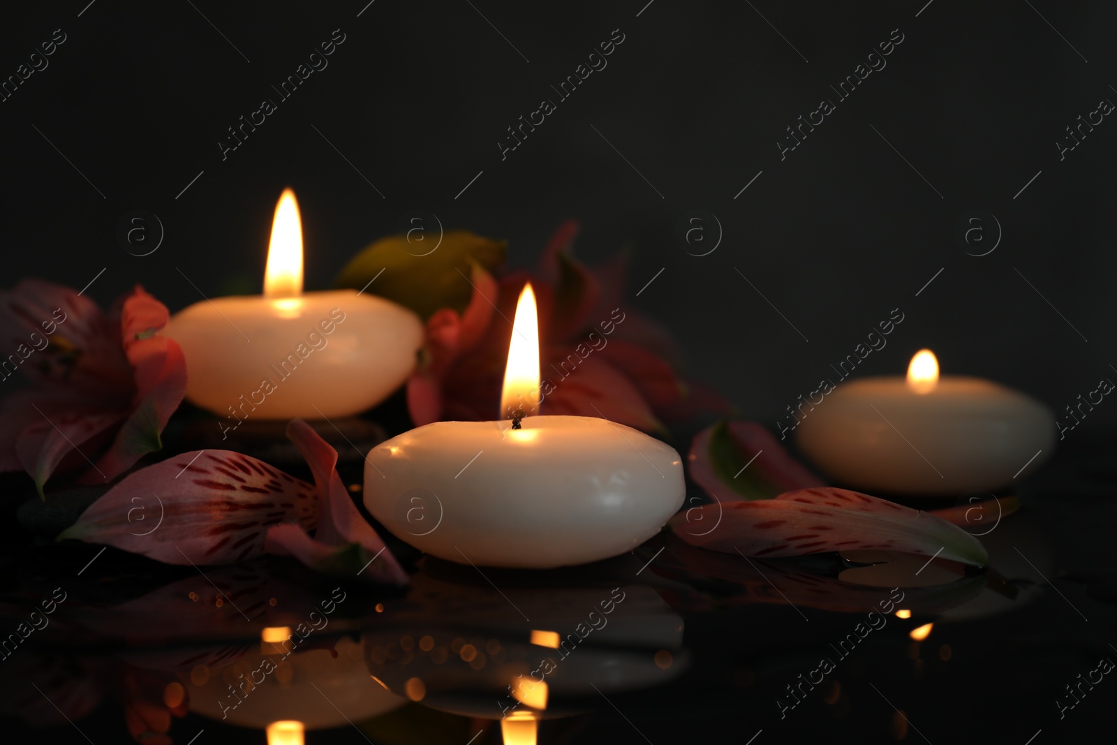 Burning candles and beautiful flowers on wet black table, closeup. Space for text Photo of Burning candles and beautiful flowers on wet black table, closeup. Space for text
