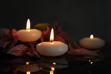Photo of Burning candles and beautiful flowers on wet black table, closeup. Space for text