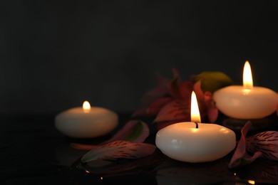 Photo of Burning candles and beautiful flowers on wet black table, closeup. Space for text