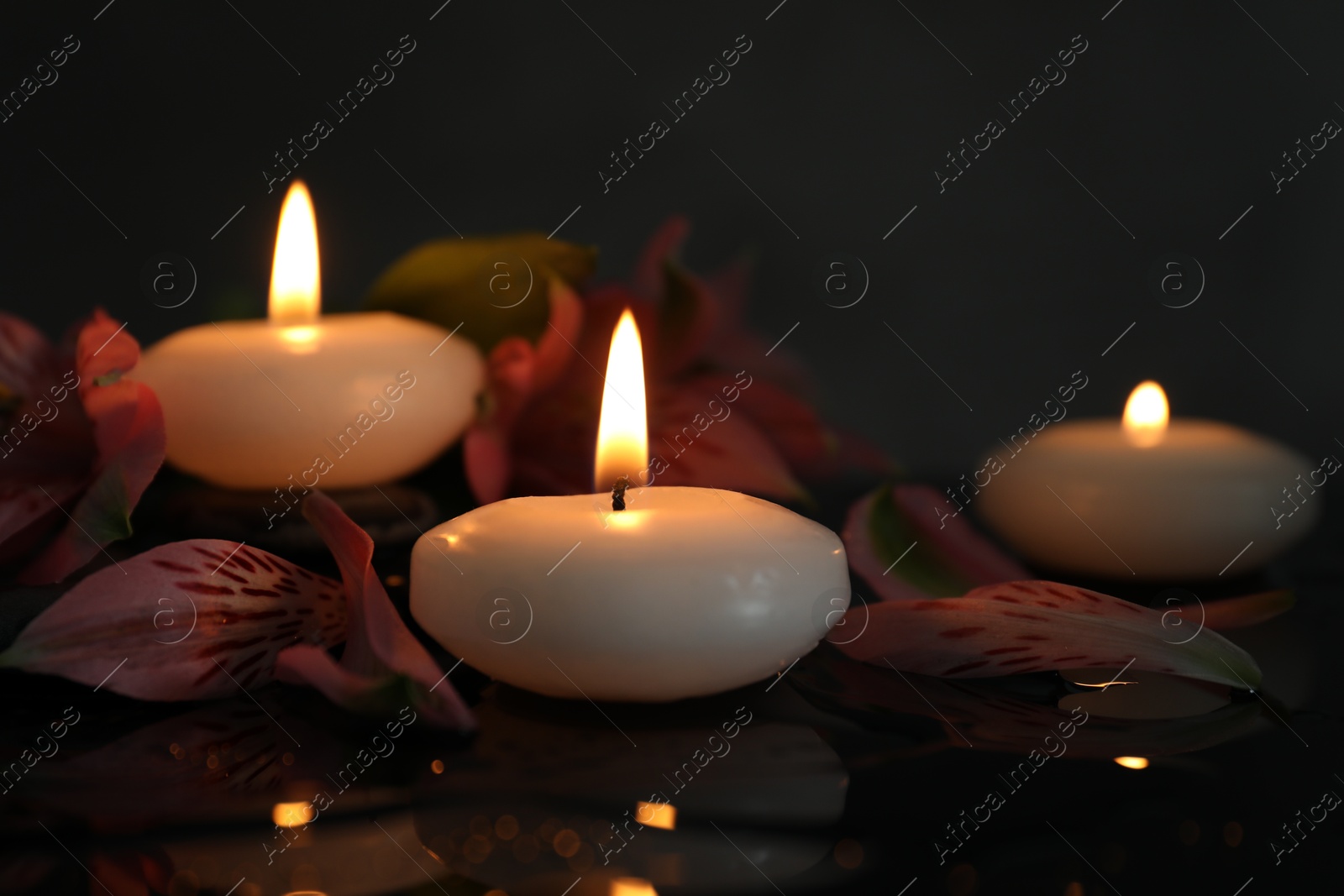 Burning candles and beautiful flowers on wet black table, closeup. Space for text Photo of Burning candles and beautiful flowers on wet black table, closeup. Space for text
