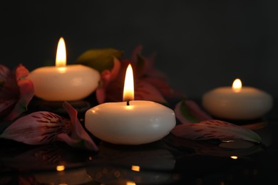Photo of Burning candles and beautiful flowers on wet black table, closeup. Space for text