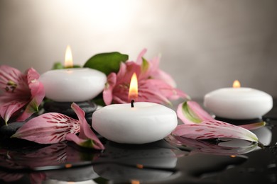 Photo of Burning candles and beautiful flowers on wet black table, closeup. Space for text