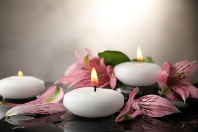 Photo of Burning candles and beautiful flowers on wet black table, closeup. Space for text