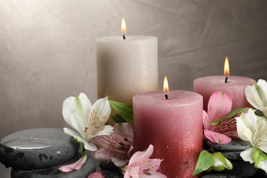 Photo of Burning candles and beautiful flowers against light background, closeup