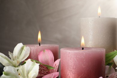 Photo of Burning candles and beautiful flowers against light background, closeup. Space for text