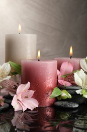 Photo of Burning candles, spa stones and beautiful flowers on wet black table, closeup