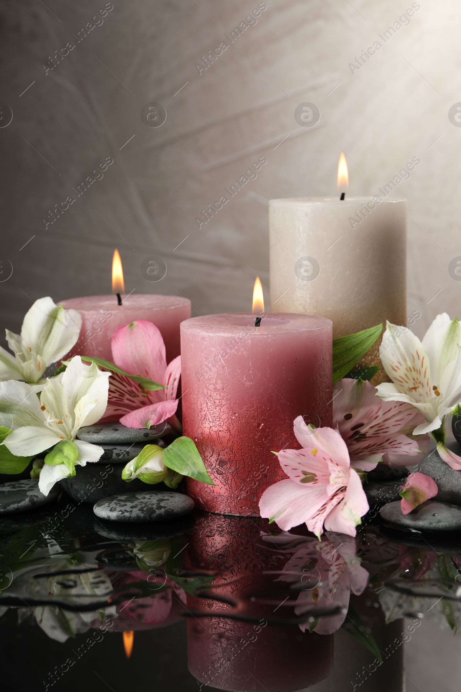 Burning candles, spa stones and beautiful flowers on wet black table Photo of Burning candles, spa stones and beautiful flowers on wet black table
