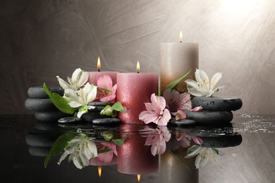 Photo of Burning candles, spa stones and beautiful flowers on wet black table