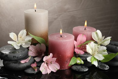 Photo of Burning candles, spa stones and beautiful flowers on wet black table, closeup