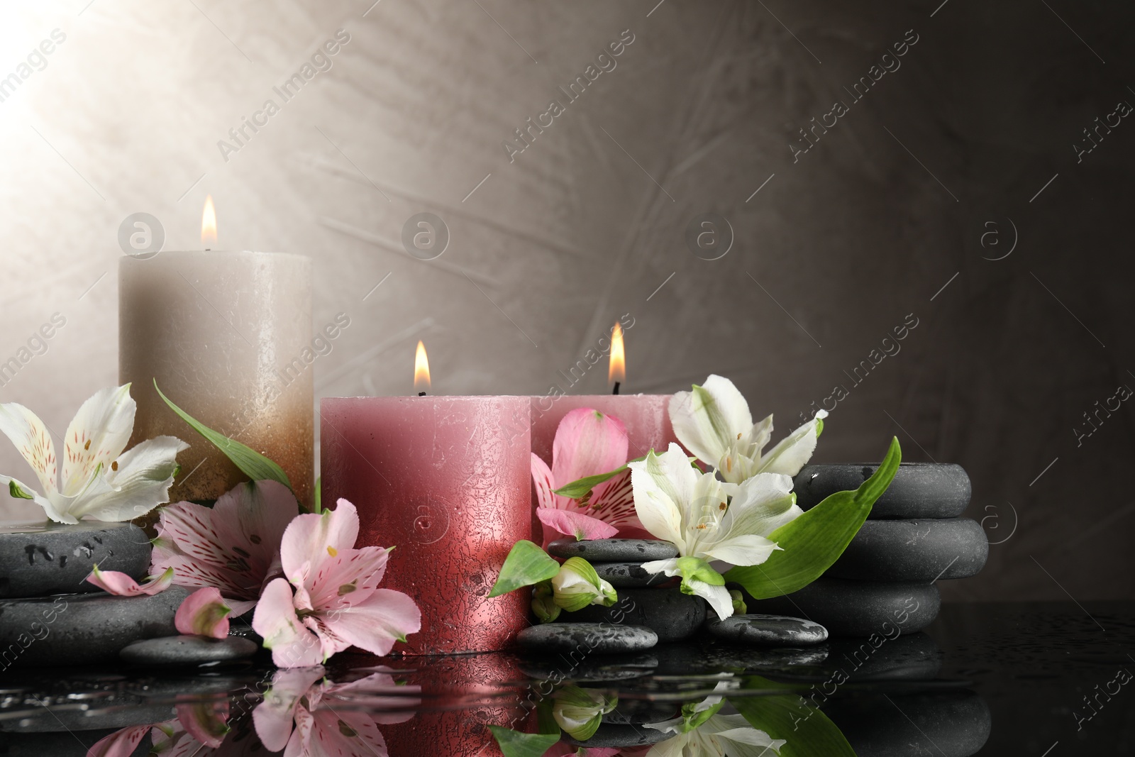 Burning candles, spa stones and beautiful flowers on wet black table. Space for text Photo of Burning candles, spa stones and beautiful flowers on wet black table. Space for text