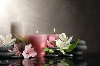 Photo of Burning candles, spa stones and beautiful flowers on wet black table. Space for text