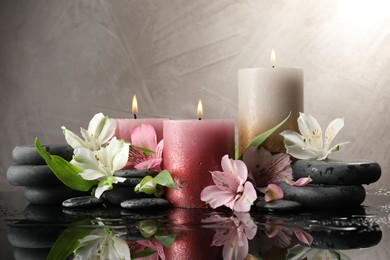 Photo of Burning candles, spa stones and beautiful flowers on wet black table