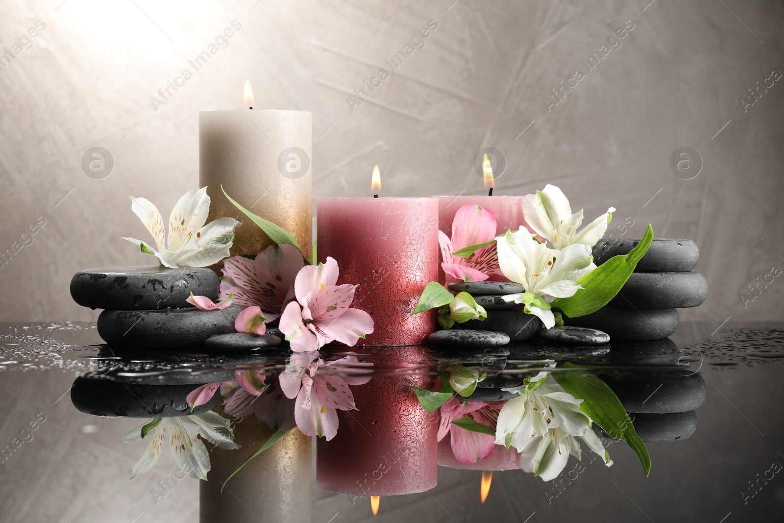Burning candles, spa stones and beautiful flowers on wet black table Photo of Burning candles, spa stones and beautiful flowers on wet black table