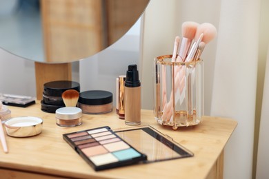 Photo of Different makeup products and brushes on vanity indoors, closeup