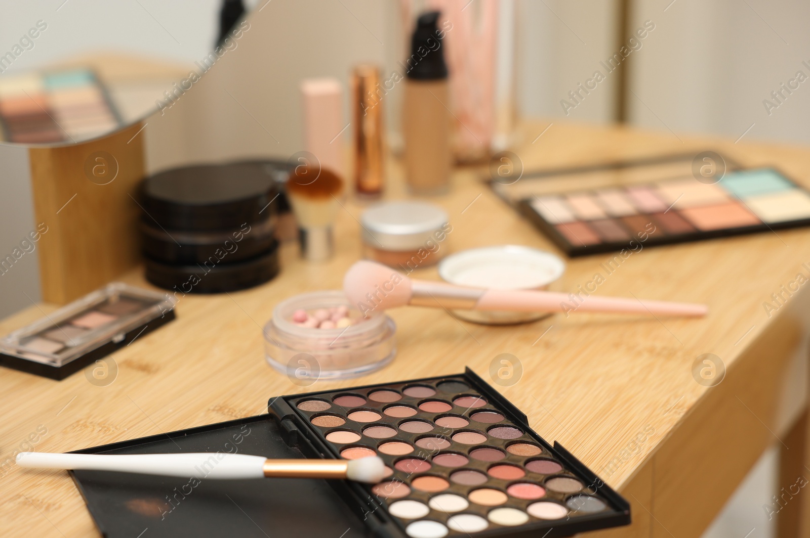 Photo of Different makeup products and brushes on vanity indoors, closeup