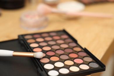 Photo of Eyeshadow palette and brush on wooden table, closeup