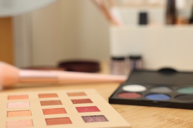 Photo of Eyeshadow palettes and brush on wooden table, closeup. Space for text