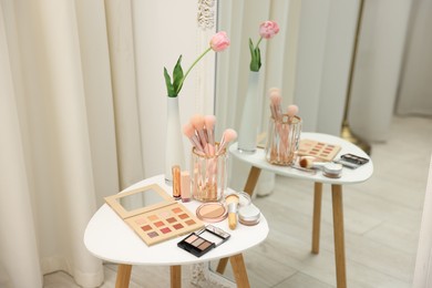 Photo of Different makeup products and brushes on white table near mirror indoors