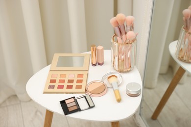 Photo of Different makeup products and brushes on white table near mirror indoors