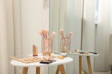 Photo of Different makeup products and brushes on white table near mirror indoors