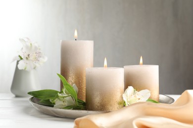 Photo of Burning candles and beautiful flowers on white table. Space for text