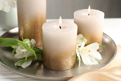 Photo of Burning candles and beautiful flowers on white table, closeup