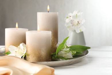 Photo of Burning candles and beautiful flowers on white table