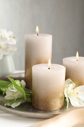 Photo of Burning candles and beautiful flowers on white table, closeup