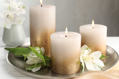 Photo of Burning candles and beautiful flowers on white table, closeup