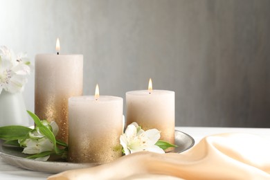 Photo of Burning candles and beautiful flowers on white table. Space for text
